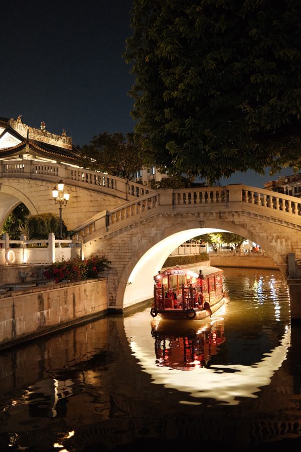 Lit stone bridge with a moon gate reflected in the canal at night